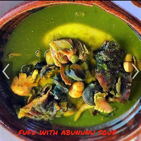 Close-up of a bowl of green Fufu with Abununu soup, featuring various meats and vegetables.