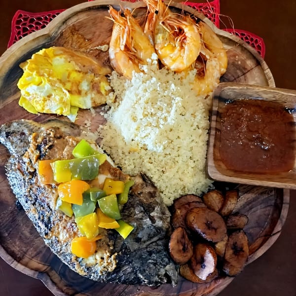 African platter with grilled fish, shrimp, couscous, plantains, scrambled eggs, and sauce.