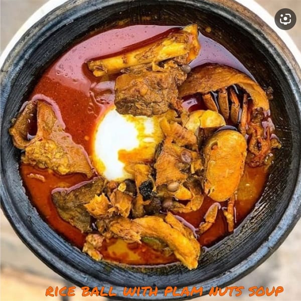 A close-up of a dark bowl filled with PRIXYS AFRICAN RESTAURANT's rice ball with palm nuts soup.