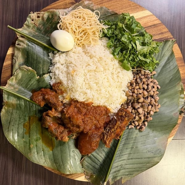 African meal on a banana leaf with rice, stewed meat, black-eyed peas, spaghetti, lettuce, and a boiled egg.