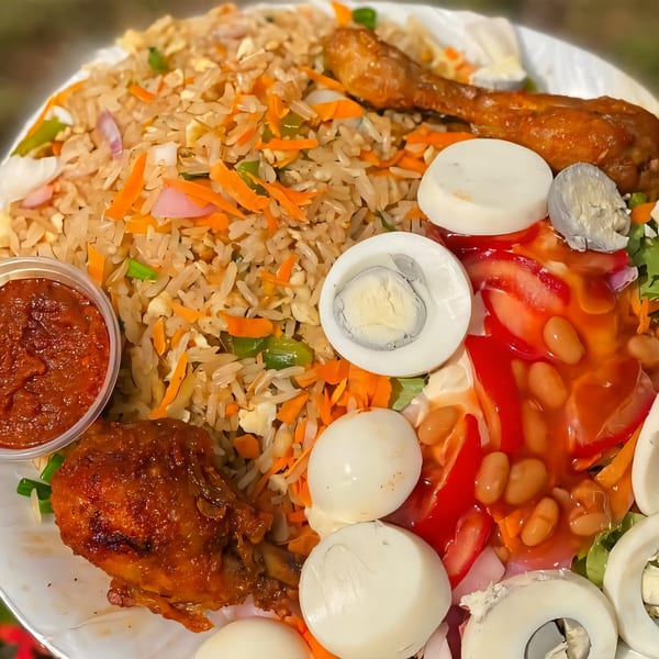 African jollof rice with chicken, hard-boiled eggs, salad, and a side of red sauce.