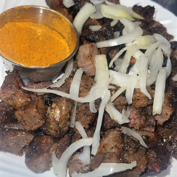 Grilled beef cubes with sliced onions and a side of orange spice powder from PRIXYS AFRICAN RESTAURANT.